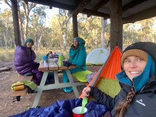 A photo of Hannah and her friends at their campsite wrapped in their sleeping bags to keep out the cold.