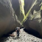 A picture of Hannah walking through an old river bed with uneven pebbles on the bottom and high walls either side.