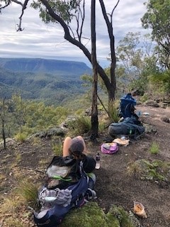 A photo of Hannah at the top of the Gorge at Carnarvon National Park looking out at the scenery. She is leaning against her backpack.