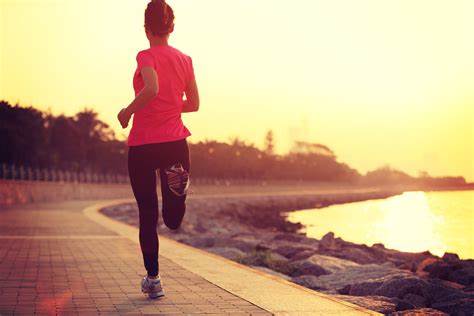 A picture of a woman running along a river at sundown.