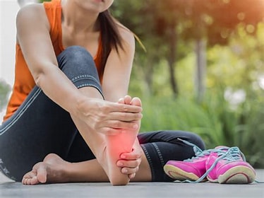 A picture of a women who has been running and taken off her shoes and holding her sore foot 